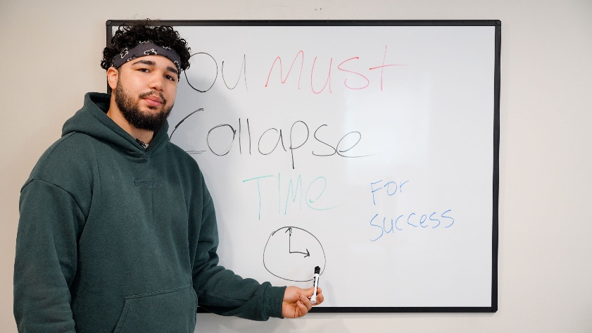 Josh Anthony stands in front of his signature message — “Collapse Time for Success” a principle at the core of his mindset coaching method.